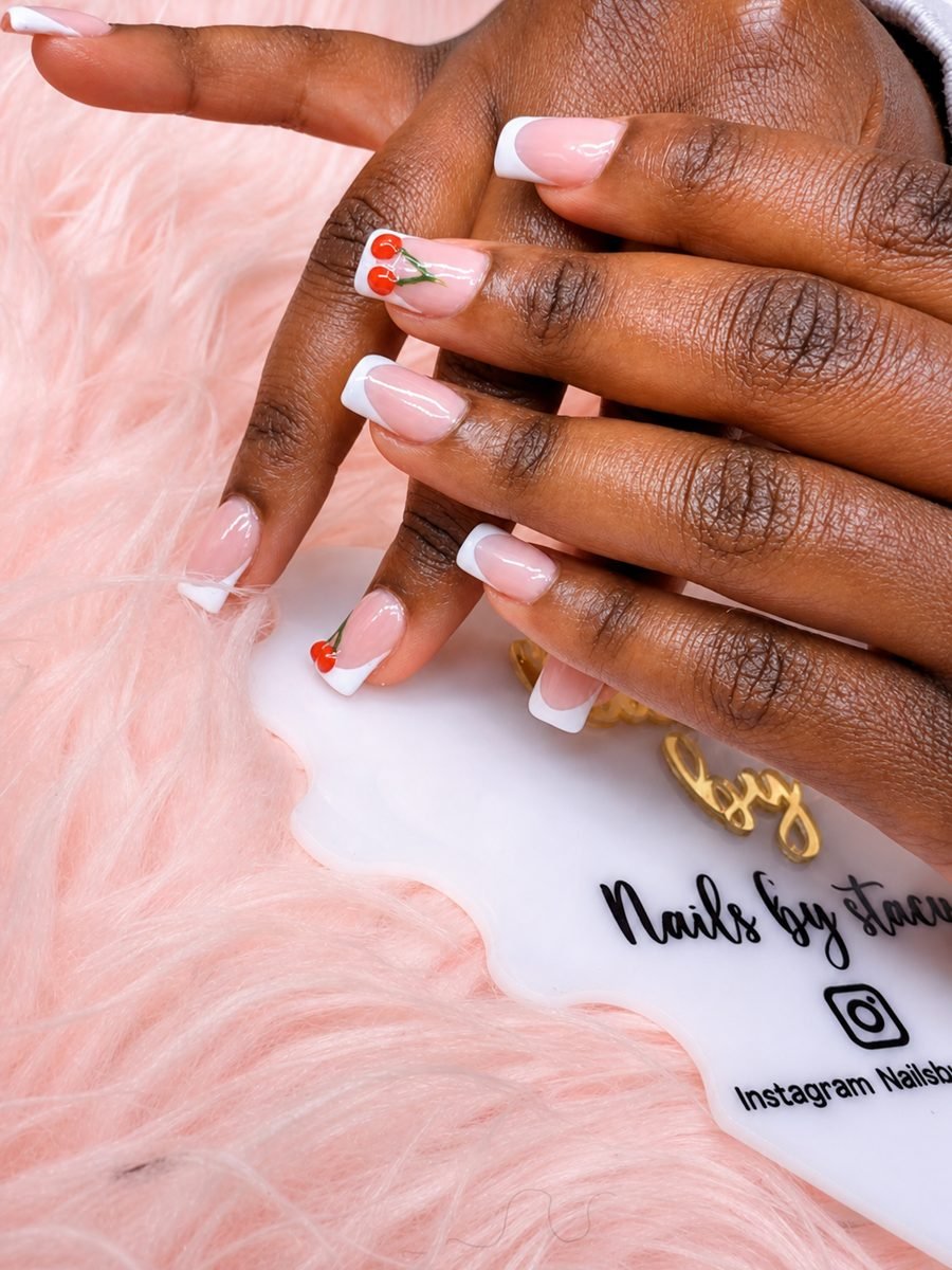White French tip nails with red cherry nail art, resting on blush fur