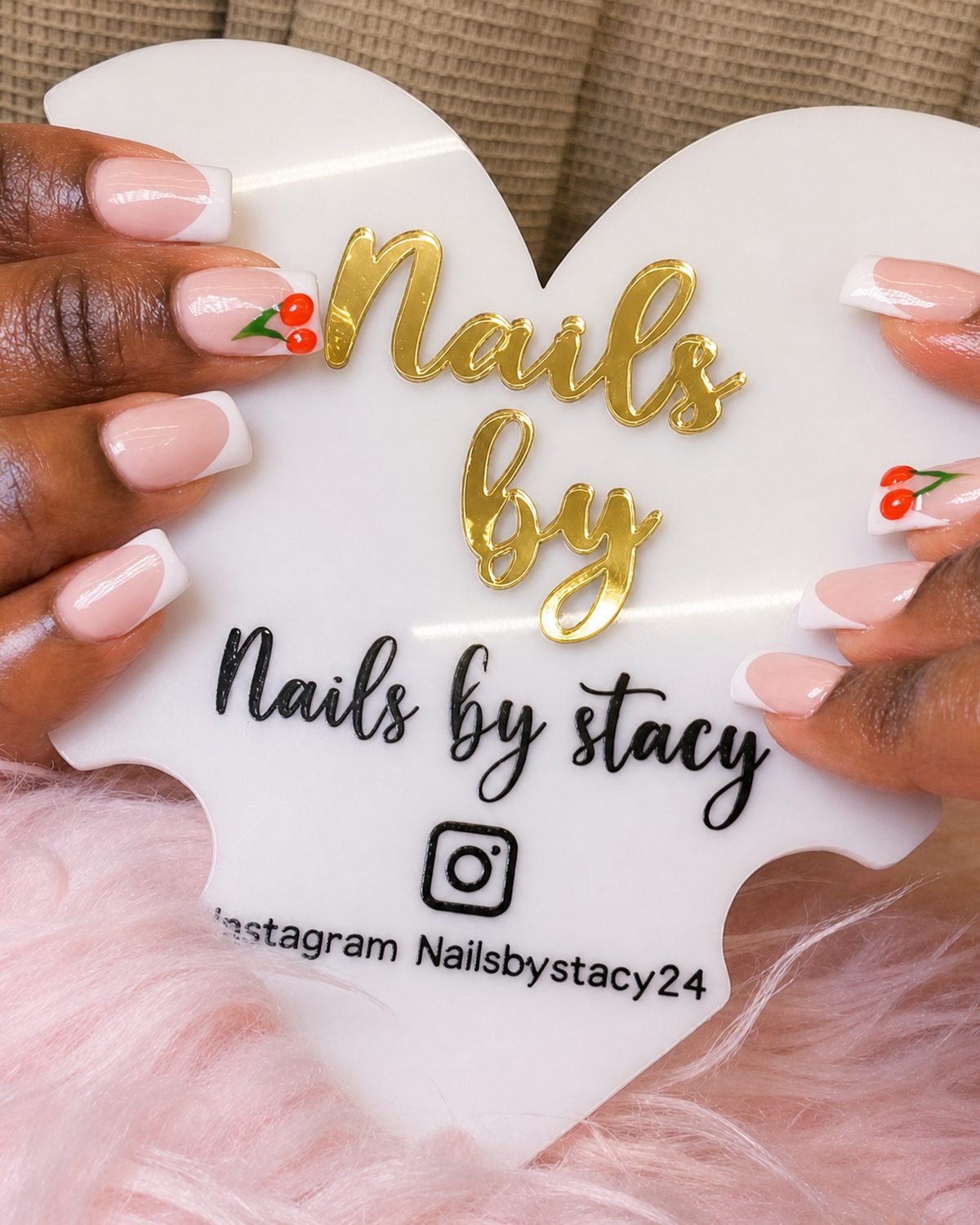 Close-up of fresh French tip nails with cherry nail art, holding the Nails by Stacy sign